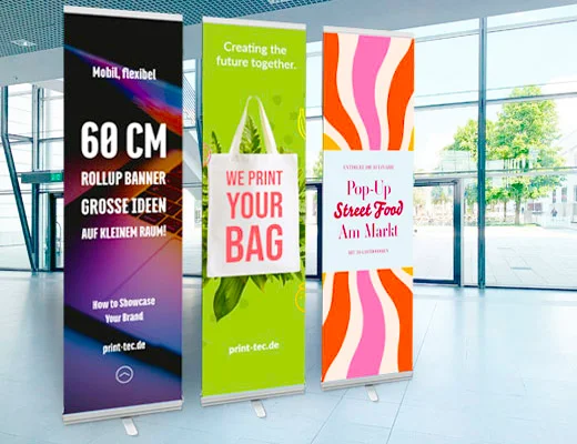 Auf dem Foto sind drei schmale Roll‑ups mit je 60 cm Breite zu sehen, die nebeneinander stehen. Jedes Roll‑up zeigt ein eigenes Motiv und Design.